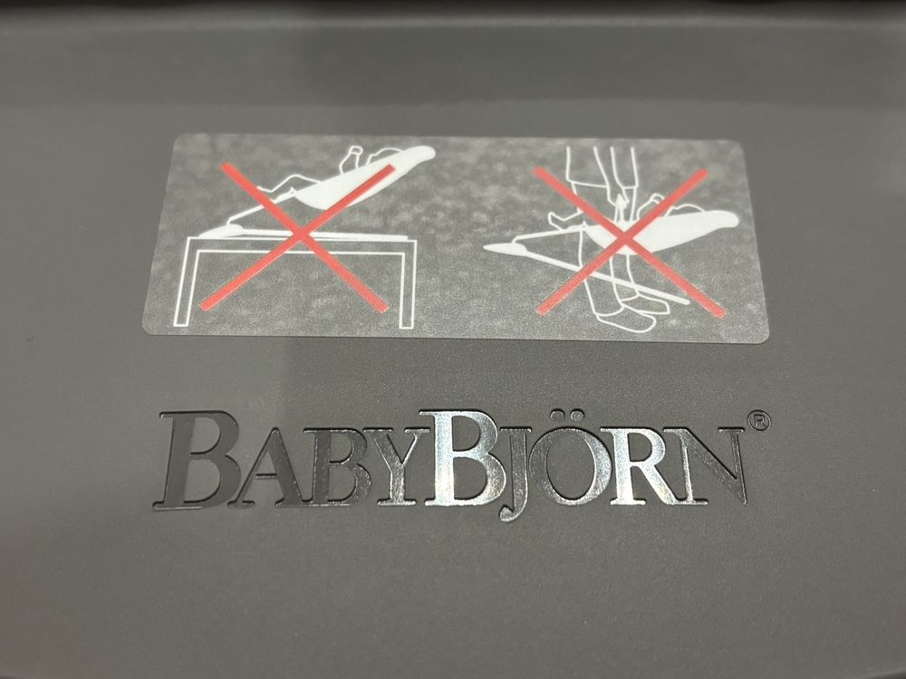 バウンサー台座の注意ステッカー。赤い×印つきの絵表示が2つと、BABYBJÖRNの刻印